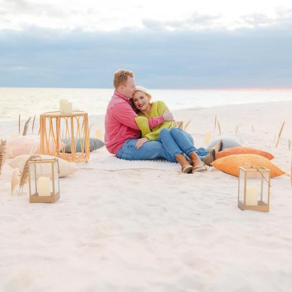 Couple enjoying a picnic blanket on the beach by Beachside Blankets after a proposal